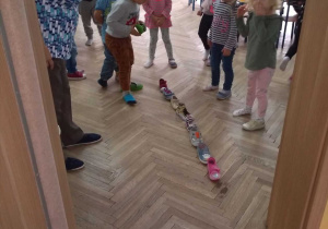 Dzieci wspólnie z nauczycielką ustawiają w rzędzie buty